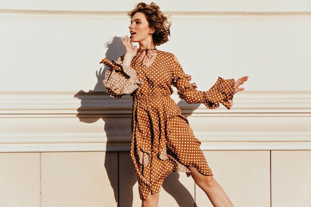 Señora alegre en traje marrón mirando a su alrededor Retrato al aire libre de la modelo caucásica de moda con peinado ondulado corto