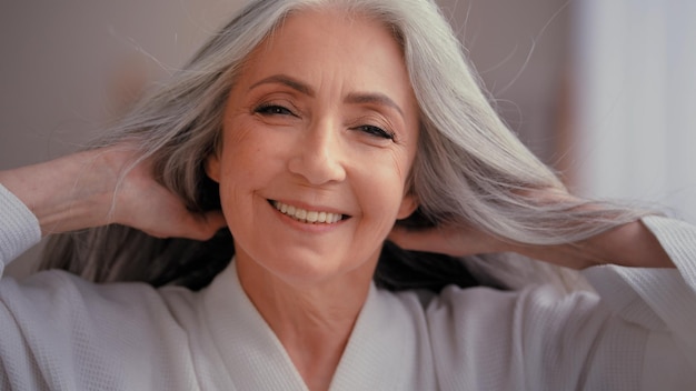 Señora de los años 50 sonriendo mirando a la cámara mimarse tocar el cabello gris disfrutar de un peinado saludable cuidado del cabello