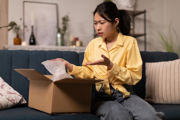 Señora asiática descontenta que desempaqueta la caja de cartón con el mal producto interior