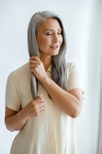 Señora asiática de mediana edad relajada en trazos de blusa mechón de cabello plateado sobre fondo claro