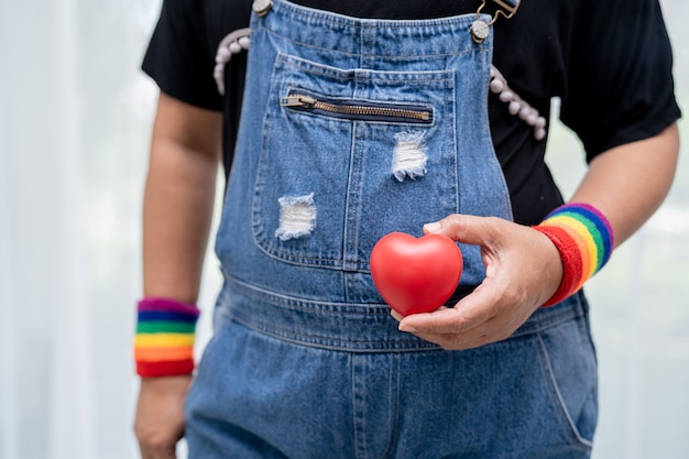 Señora asiática con pulseras con la bandera del arco iris y mantenga el símbolo del corazón rojo del mes del orgullo LGBT