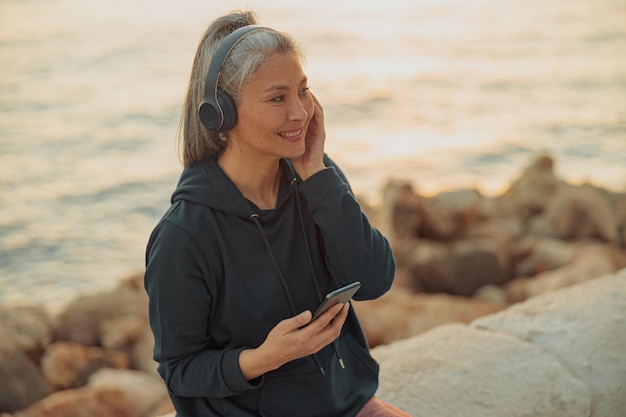 Señora asiática sentada junto al mar en auriculares