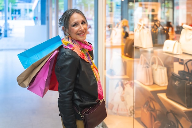 Señora atractiva con bolsas de compras feliz sonriendo mirando a la cámara frente a una tienda