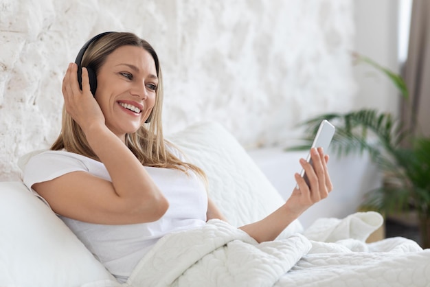 Señora bonita positiva que tiene videollamadas con teléfono inteligente y auriculares