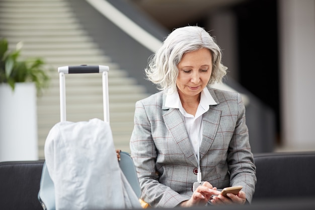 Señora de cabello gris revisando mensajero en el aeropuerto