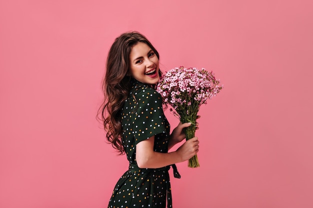 Foto señora con cabello ondulado sonriendo y sosteniendo flores en la pared rosa