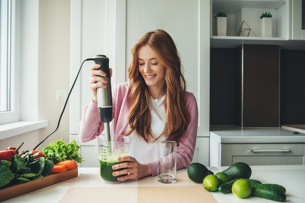 Señora caucásica de jengibre con pecas haciendo jugo de limón y aguacate con un exprimidor eléctrico