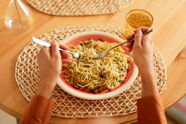 Señora comiendo sabrosa pasta italiana con queso parmesano sosteniendo un tenedor y una cuchara de espagueti enrollándolo alrededor