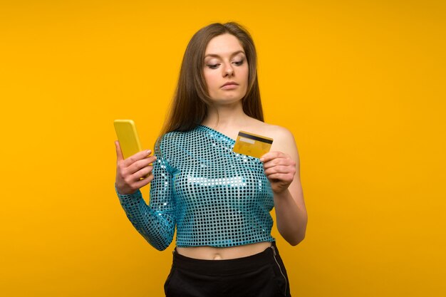 Señora comprando en línea con una tarjeta de crédito y un teléfono inteligente sobre fondo amarillo