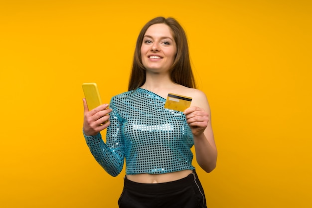 Señora comprando en línea con una tarjeta de crédito y un teléfono inteligente sobre fondo amarillo