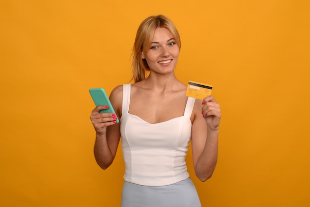 Señora comprando en línea con una tarjeta de crédito y un teléfono inteligente sobre fondo amarillo