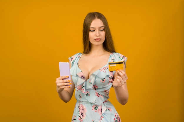 Señora comprando en línea con una tarjeta de crédito y un teléfono inteligente sobre fondo amarillo