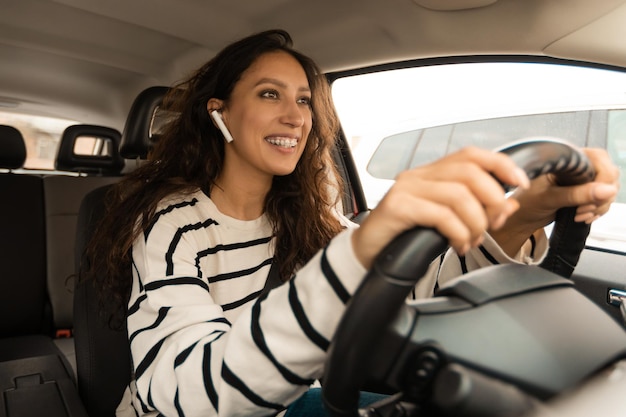 Señora conduciendo sentada en automóvil escuchando música en auriculares