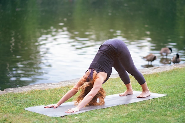 Señora deportiva haciendo yoga al aire libre en el parque cerca del agua