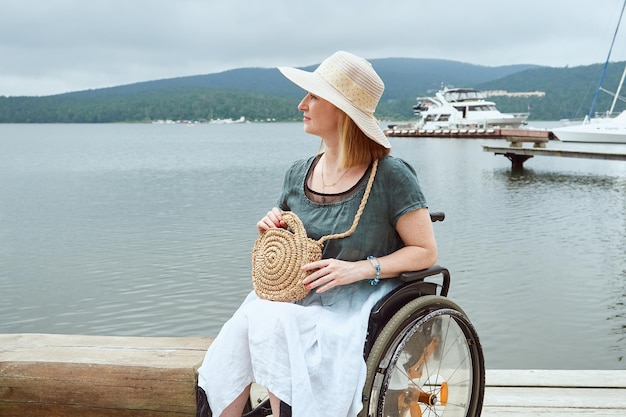 Una señora con discapacidad en un sombrero disfruta de un día de verano mientras camina cerca del mar