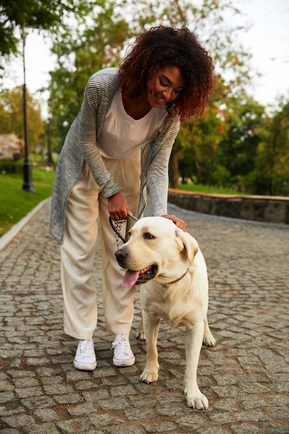 Señora feliz abrazando a su perro blanco amigable mientras camina en el parque