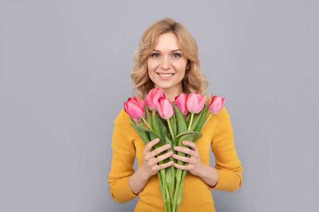 Señora feliz sostener flores para vacaciones de primavera sobre fondo gris