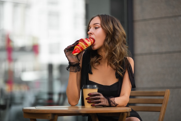 Señora hambrienta desayunando con croissant en un café