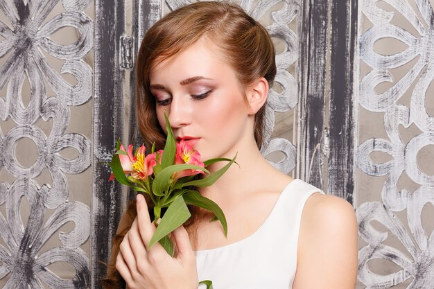 Señora hermosa joven con flores sobre fondo gris