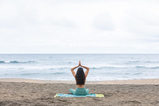 Señora irreconocible sentada en Lotus asana y meditando en la playa