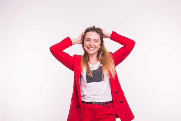 Señora joven feliz en chaqueta roja corrige su cabello sobre fondo blanco.