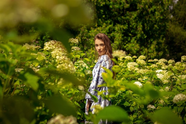 Señora joven glamour con los ojos cerrados posando en el campo de flores en vestido con estampado