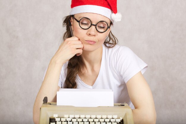 Señora joven con sombrero de Santa Claus cerca de la máquina de escribir.