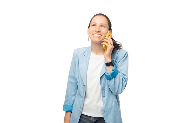 Señora joven sonriente está hablando por teléfono mientras está de pie sobre fondo blanco.