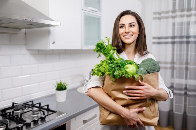Señora joven sonriente posando con sus compras de verduras