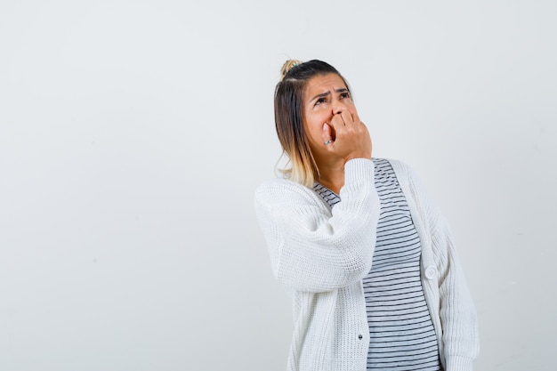 Foto señora linda en camiseta, cardigan mordiéndose las uñas, mirando hacia arriba y mirando preocupado, vista frontal.