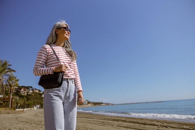 Señora madura elegante de pie al aire libre frente al mar