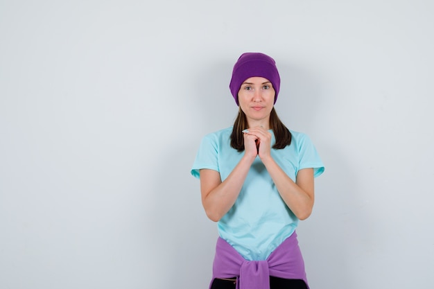 Señora maravillosa con las manos en gesto de oración en blusa, gorro y mirando esperanzado. vista frontal.