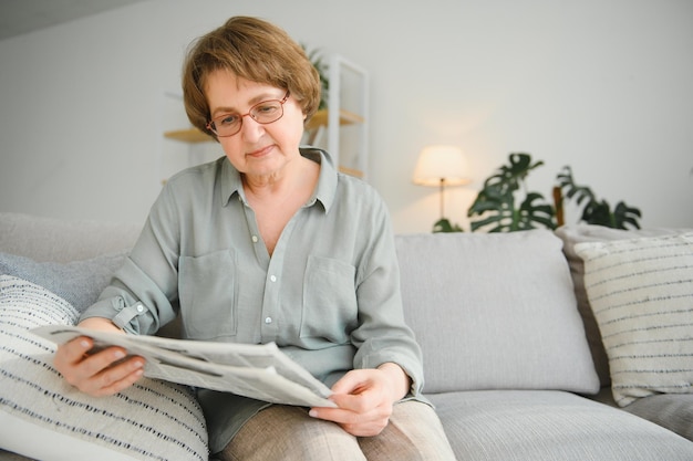 Señora mayor leyendo su periódico en casa relajándose en un sofá y mirando por encima del espectador