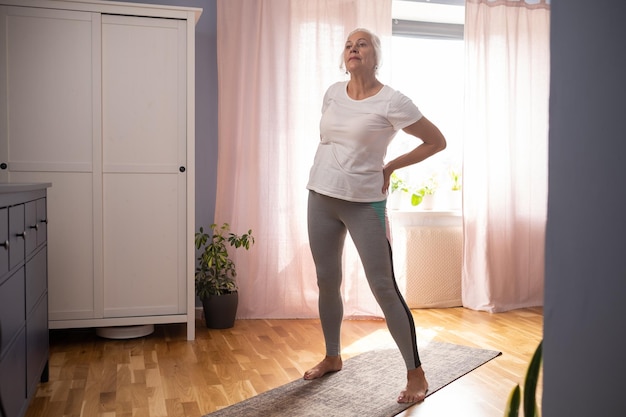 Señora mayor que hace yoga asana en la sala de estar