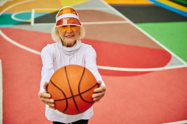 Señora mayor, saludable y alegre con pelota de baloncesto en una colorida plaza al aire libre