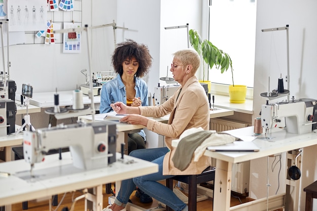 Señora de mediana edad con asistente afroamericano juntos en el trabajo sobre la ropa en el estudio