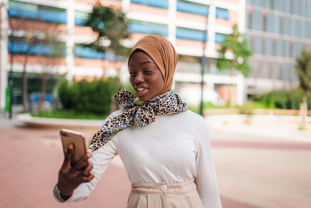 Señora musulmana negra sonriente revisando el mensaje en el teléfono inteligente