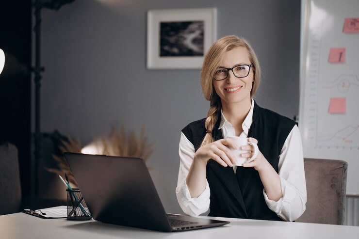Señora de negocios bebiendo café mientras trabaja en la computadora portátil