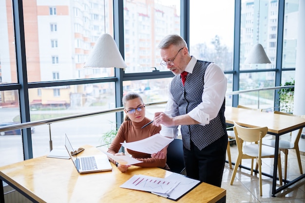 Señora de negocios chica sentada en una mesa de madera con una computadora portátil y discutiendo un nuevo proyecto con su maestro mentor jefe. Nuevo concepto de desarrollo empresarial