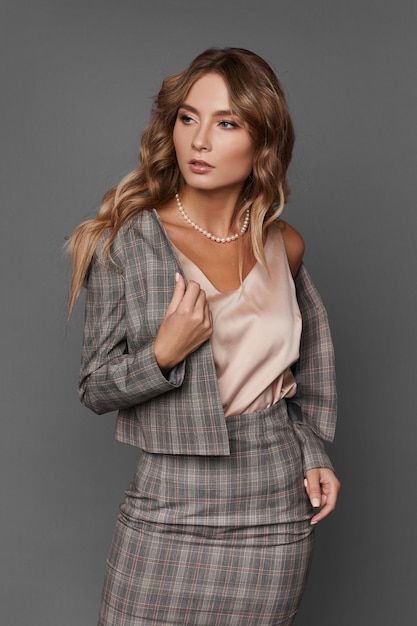 Señora de negocios elegante en el traje a cuadros y la blusa de satén mirando a un lado y posando sobre el fondo gris, aislado.