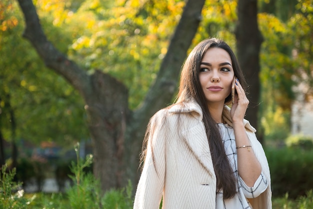 Señora de negocios habla por teléfono en otoño en el parque.