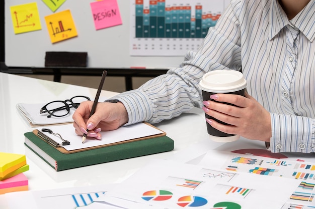 Señora de negocios de marketing en camisa a rayas en la oficina con gafas en el escritorio sosteniendo una taza de papel negro