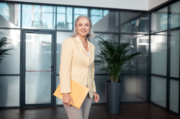 Señora de negocios. Sonriente mujer de negocios senior en elegante ropa de oficina sosteniendo una carpeta de papel mientras mira delante de ella