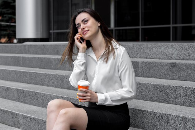 Señora de la oficina joven hermosa dice en el teléfono sonríe y bebe café