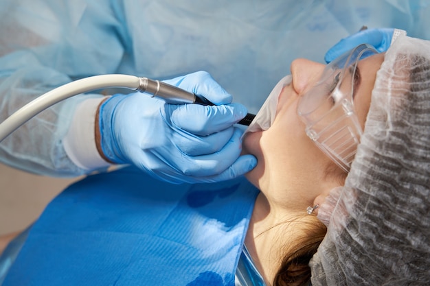 Señora paciente sentada en la silla de estomatología, diente de perforación del dentista, clínica moderna