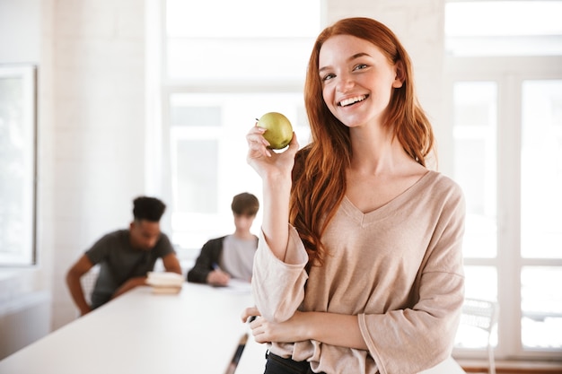 Señora pelirroja joven feliz mirando a cámara con manzana