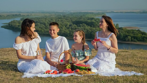 Señora positiva con hijas e hijo en la orilla del río en un picnic