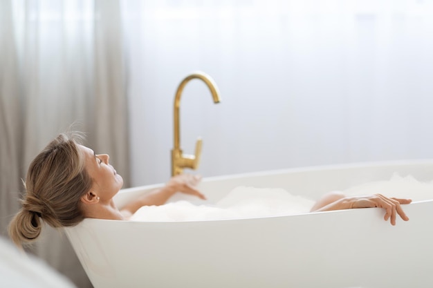 Señora relajada disfrutando de un baño aromático espumoso en casa