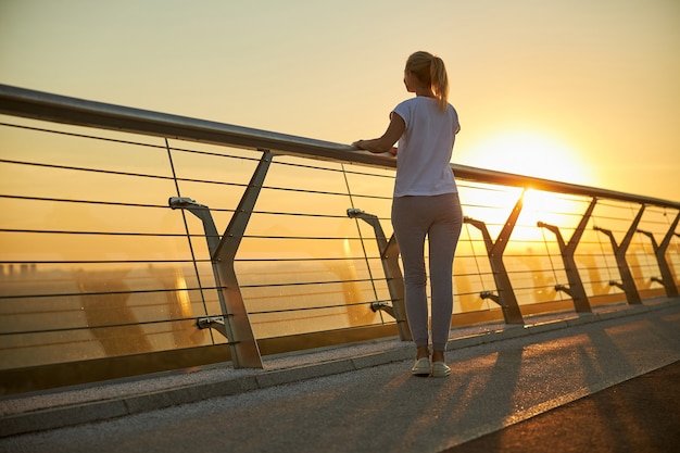 Señora rubia en ropa deportiva disfrutando de la vista del amanecer brillante mientras pasa tiempo al aire libre