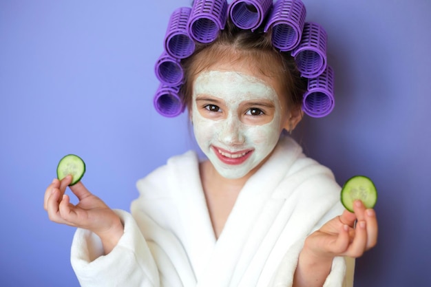 Señora con rulos en mascarilla de arcilla para el cabello en la cara con rodajas de pepino